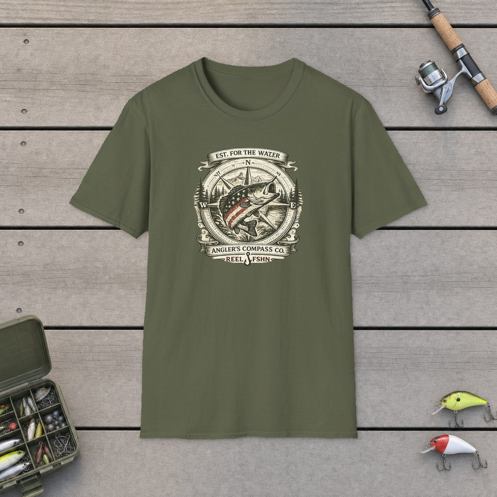 Angler's Compass Company T-Shirt flat-laid on wooden dock boards beside a fishing rod and tackle box