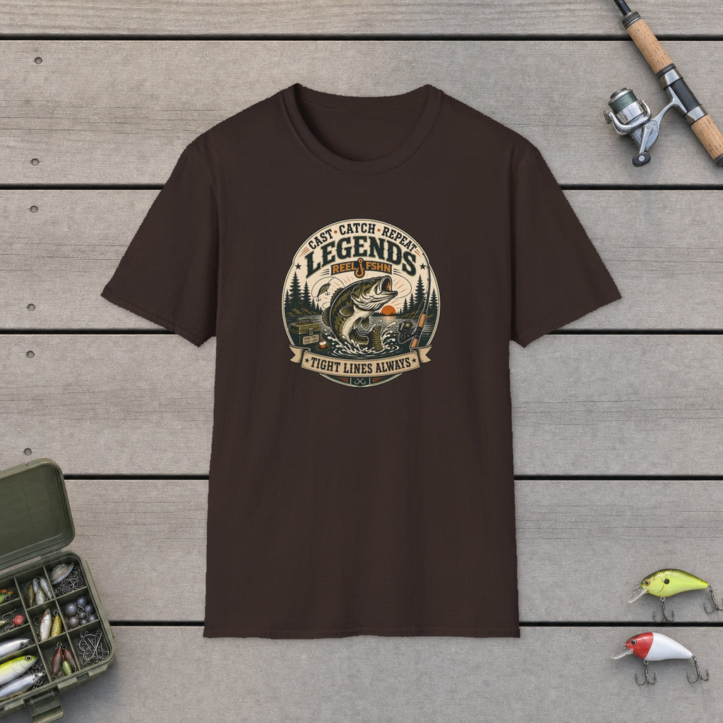 Cast Catch Repeat Legends T-Shirt flat-laid on wooden dock boards beside a fishing rod and tackle box