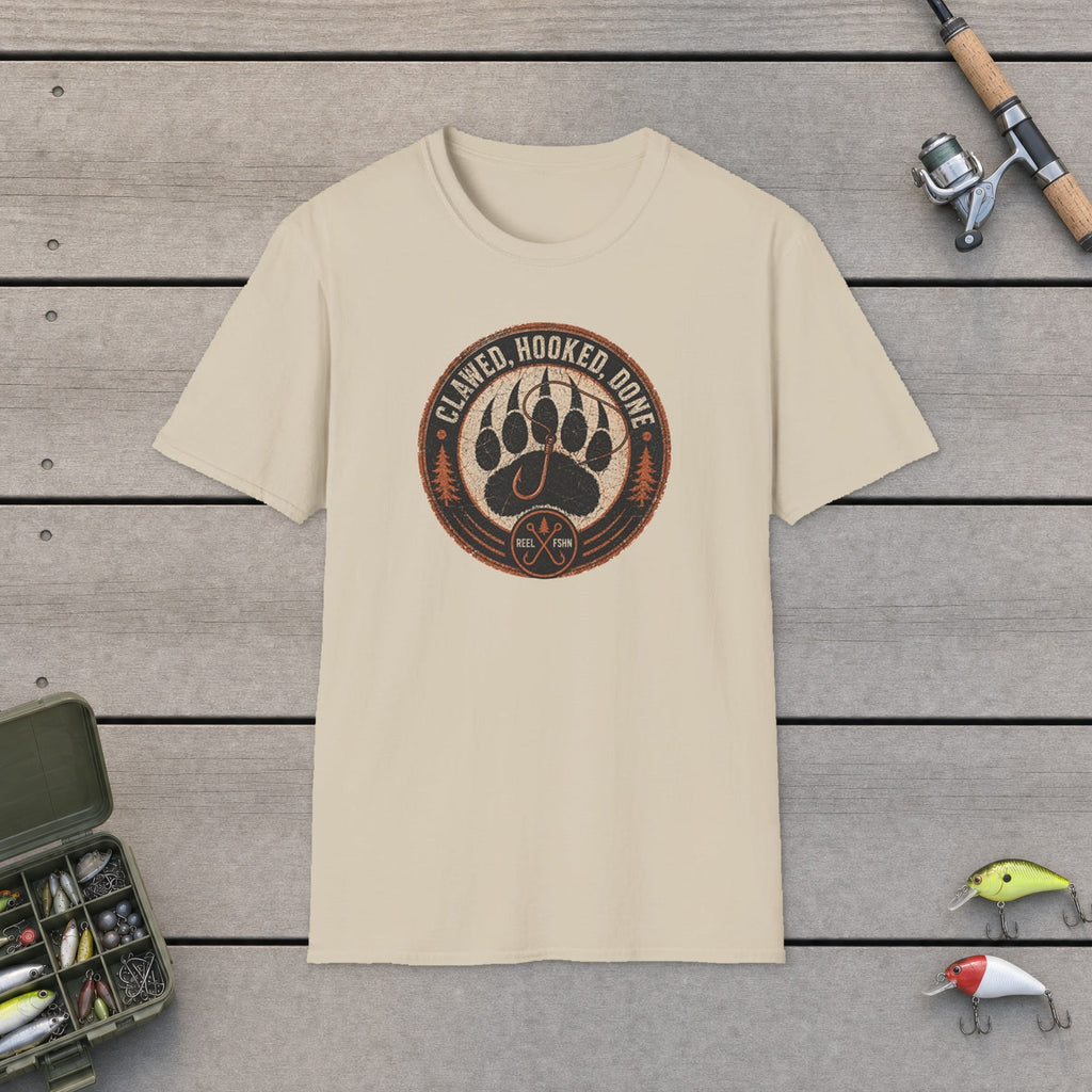Clawed Hooked Done T-Shirt flat-laid on wooden dock boards beside a fishing rod and tackle box