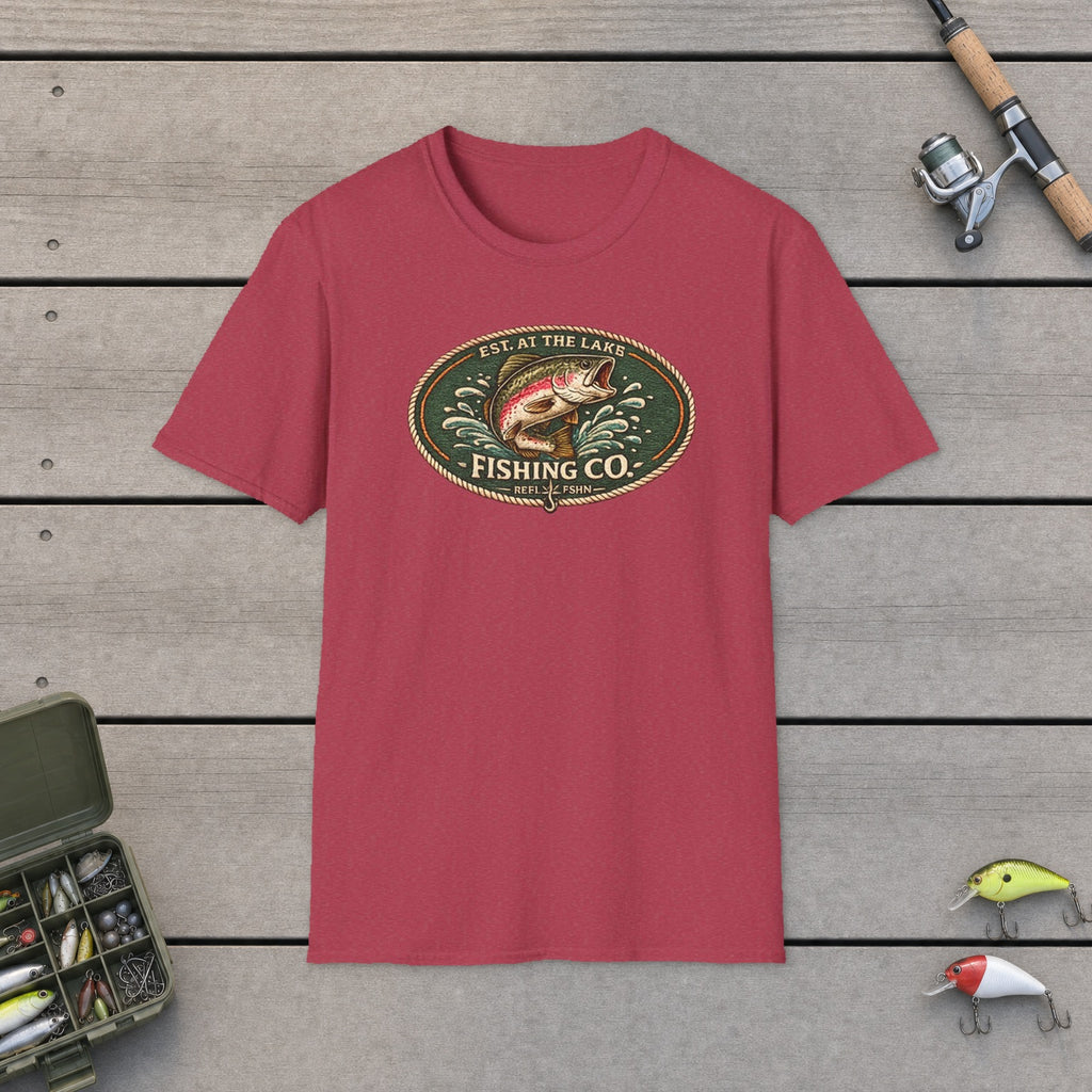 Est. At The Lake Fishing Co. T-Shirt flat-laid on wooden dock boards beside a fishing rod and tackle box