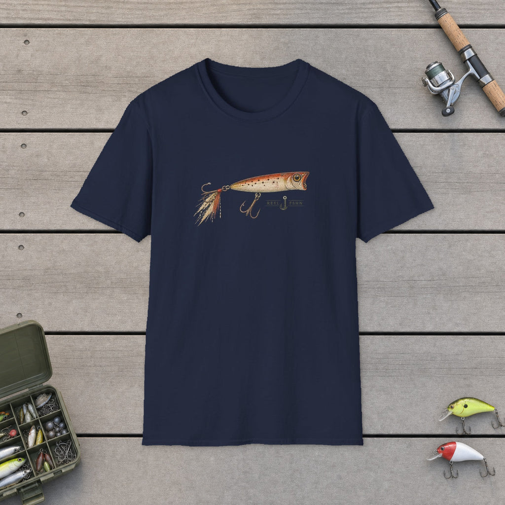 Fishing Lure T-Shirt flat-laid on wooden dock boards beside a fishing rod and tackle box