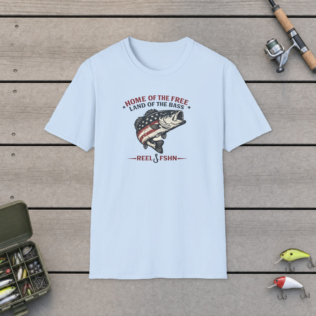 Home Of The Free Land Of The Bass T-Shirt flat-laid on wooden dock boards beside a fishing rod and tackle box