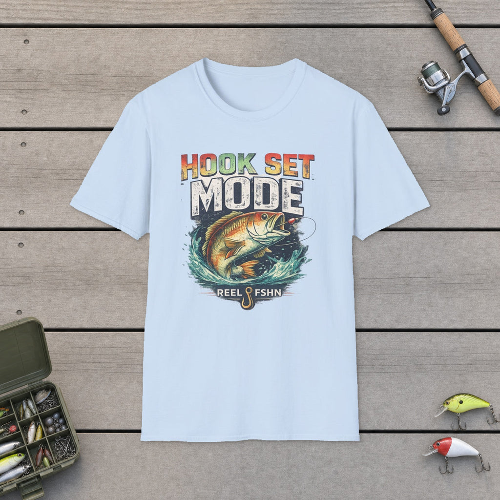 Hook Set Mode T-Shirt flat-laid on wooden dock boards beside a fishing rod and tackle box