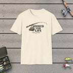 Hooked For Life T-Shirt on a wooden dock with fishing rod, reel, tackle box and lures