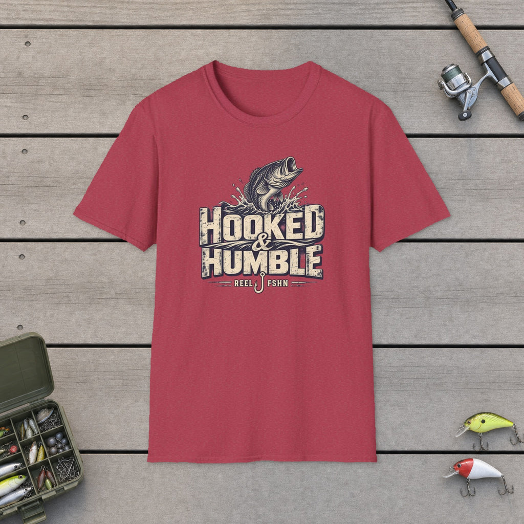 Hooked & Humble T-Shirt flat-laid on wooden dock boards beside a fishing rod and tackle box