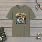 Muskie of a Thousand Casts T-Shirt on a wooden dock with fishing rod, reel, tackle box and lures
