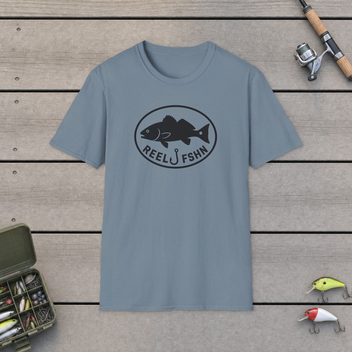 Redfish Oval Badge T-Shirt on a wooden dock with fishing rod, reel, tackle box and lures