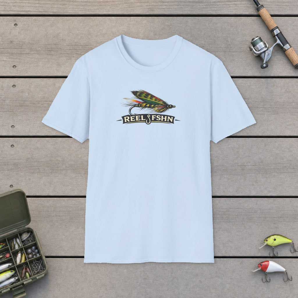 REEL FSHN FLY LURE T-Shirt flat-laid on wooden dock boards beside a fishing rod and tackle box