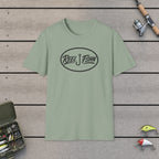 REEL FSHN Oval Badge T-Shirt on a wooden dock with fishing rod, reel, tackle box and lures